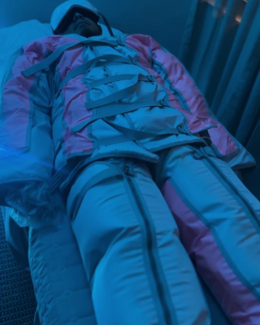 Client relaxing in a full-body pressotherapy suit under soft colored light